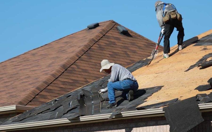 Roofers removing old asphalt shingles from the roof of a residential house; Roofing in summer. Tearing down the old roof.